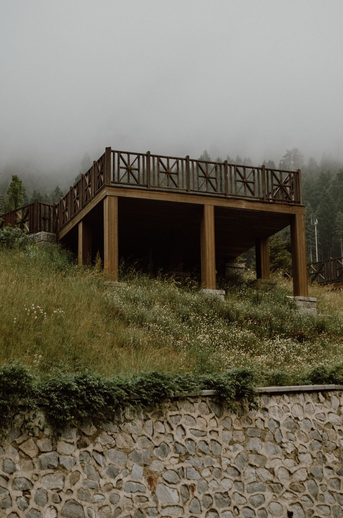 Natural wooden deck with cross-braced railings overlooking a misty forested mountain setting — illustrative image