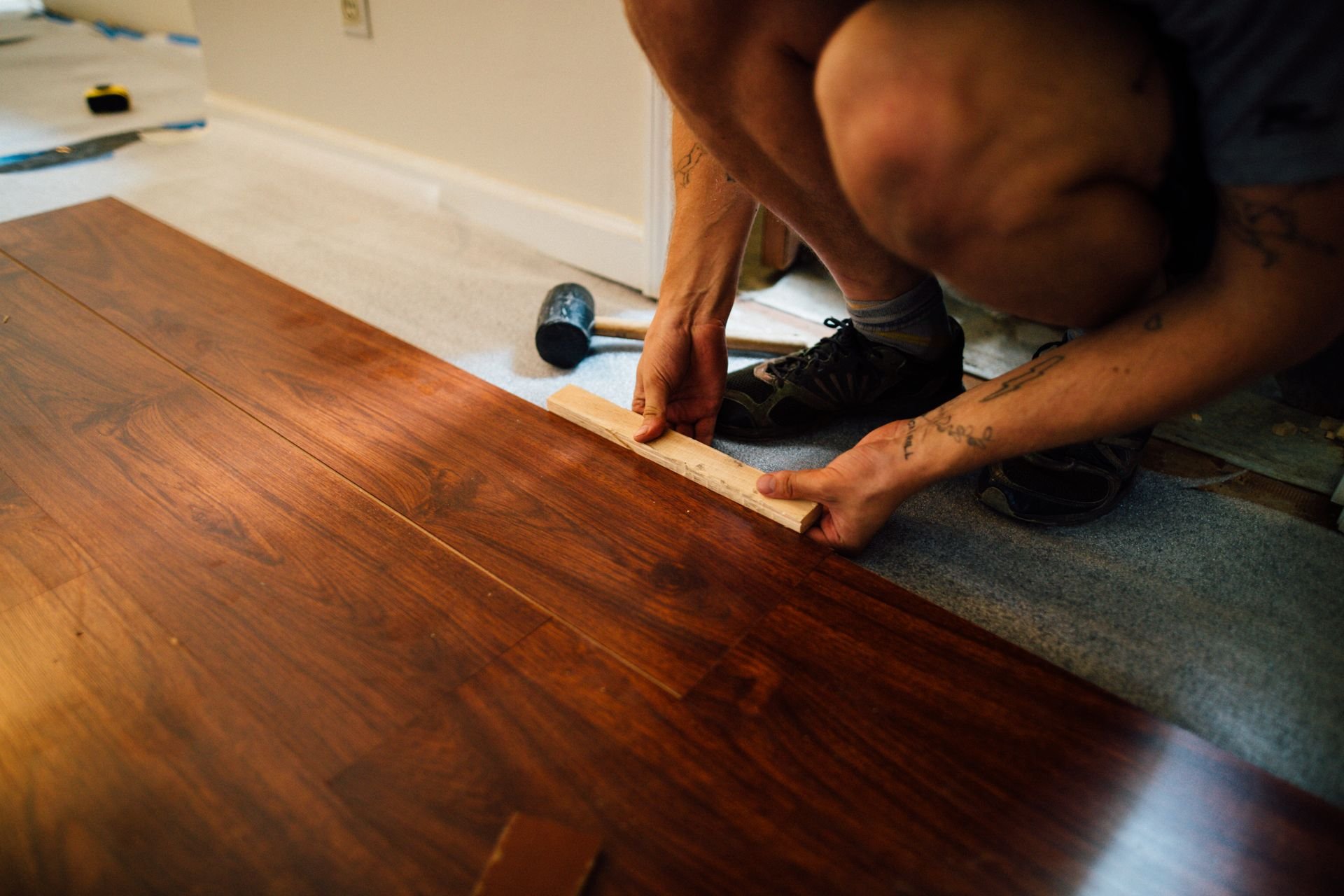 Worker fitting laminate flooring beside a residential wall — illustrative image