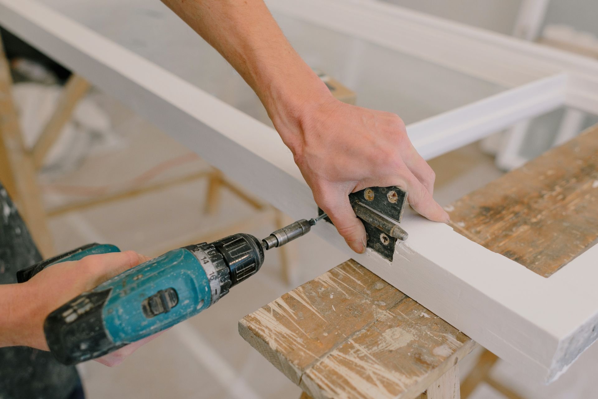 Worker fastening a door hinge with a cordless drill — illustrative image